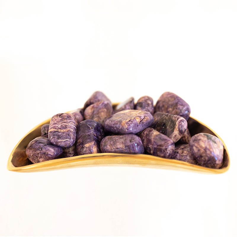 Tumbled charoite and tinaksite stones from Sacred Light Soundbaths and Crystals, showcasing vibrant purple and blue mineral patterns.