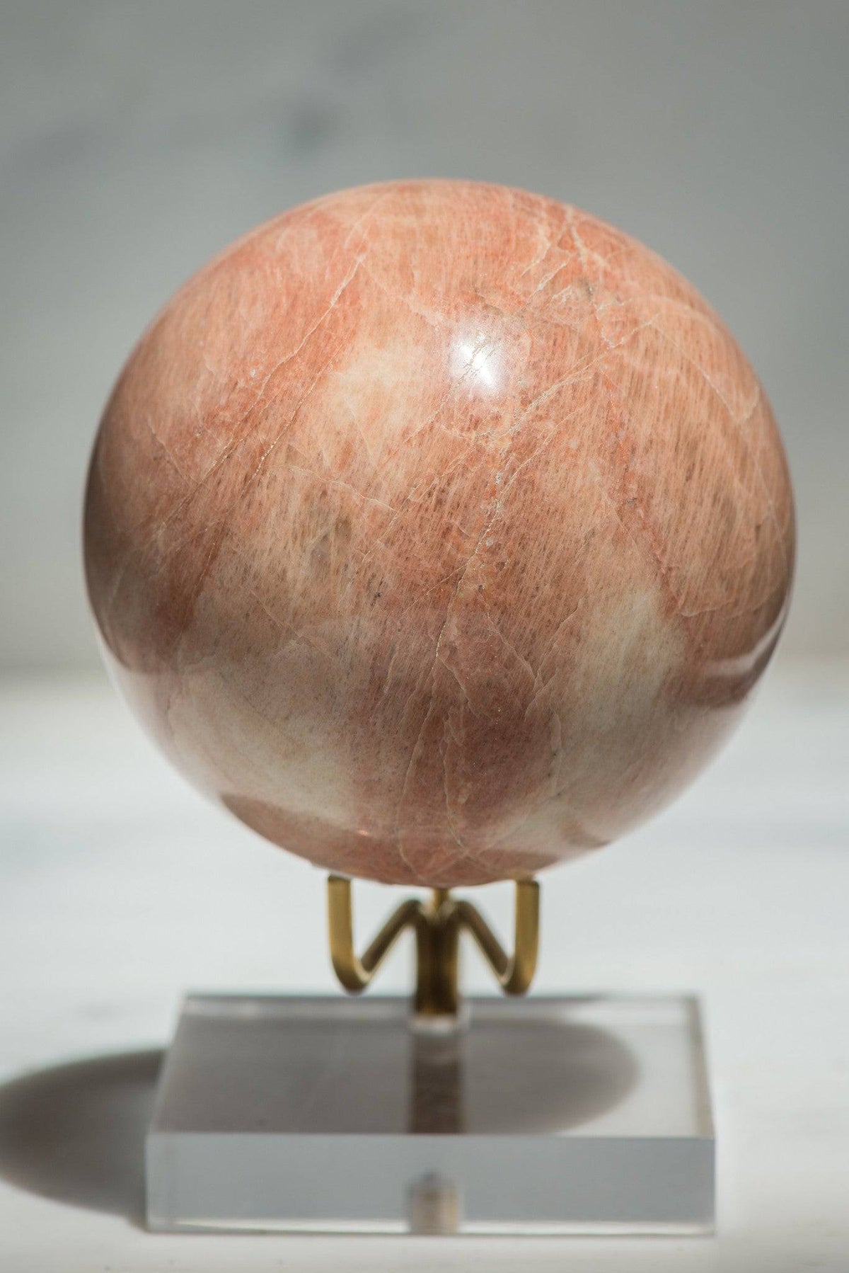 Large peach moonstone sphere from Sacred Light Soundbaths and Crystals, showcasing smooth, rounded stone with soft peach tones.