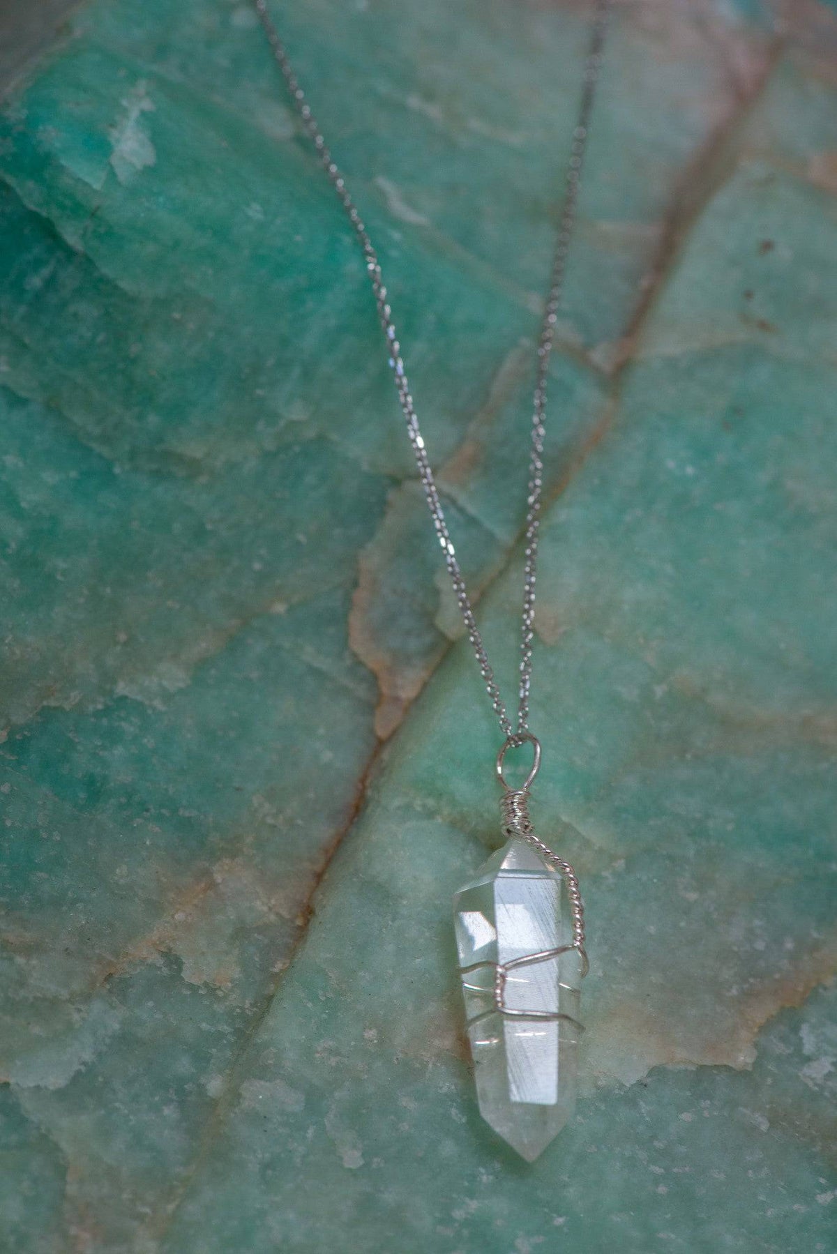 Wire wrapped clear quartz point necklace featuring a polished crystal pendant on a silver chain, handcrafted jewelry by Sacred Light.