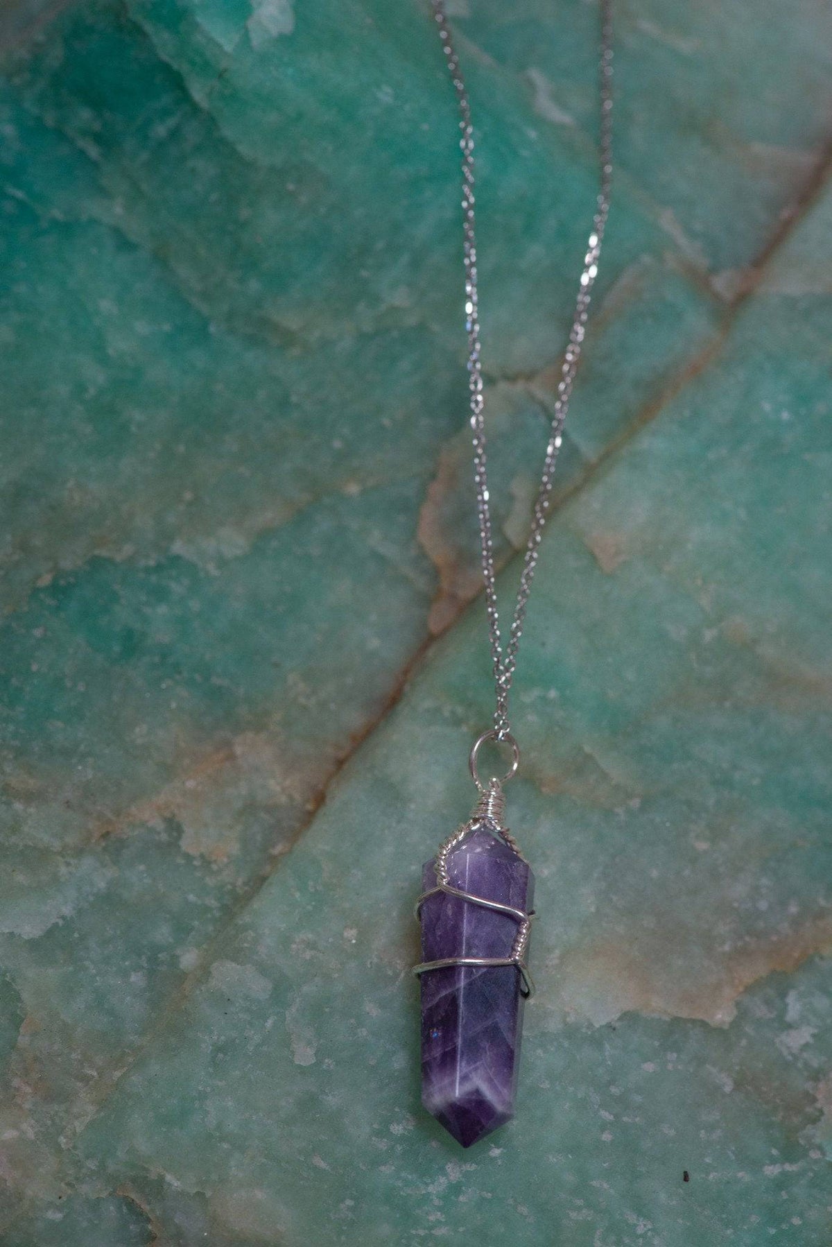 Amethyst wire-wrapped pendant jewelry featuring a polished purple gemstone on a silver chain against a neutral background.
