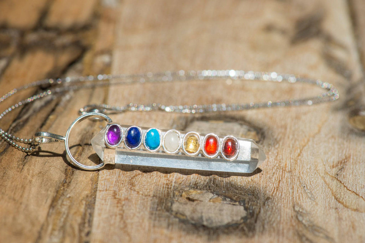 Polished chakra crystals on a clear quartz point necklace from Sacred Light Soundbaths and Crystals, showcasing vibrant gemstone colors.