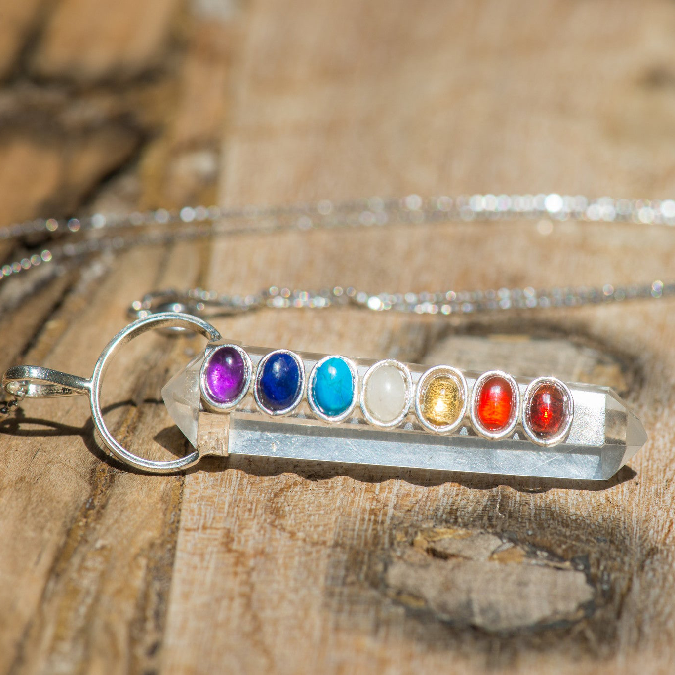 Polished chakra crystals on a clear quartz point pendant necklace by Sacred Light Soundbaths and Crystals, jewelry accessory.