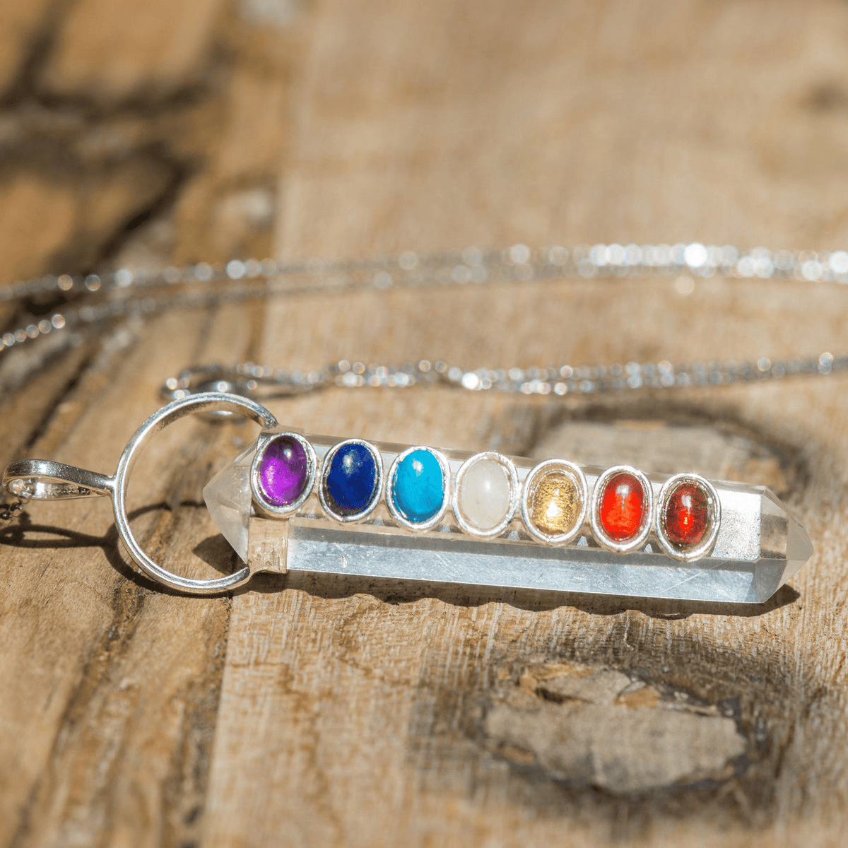 Polished chakra crystals on a clear quartz point necklace featuring vibrant, colorful stones from Sacred Light Soundbaths and Crystals.