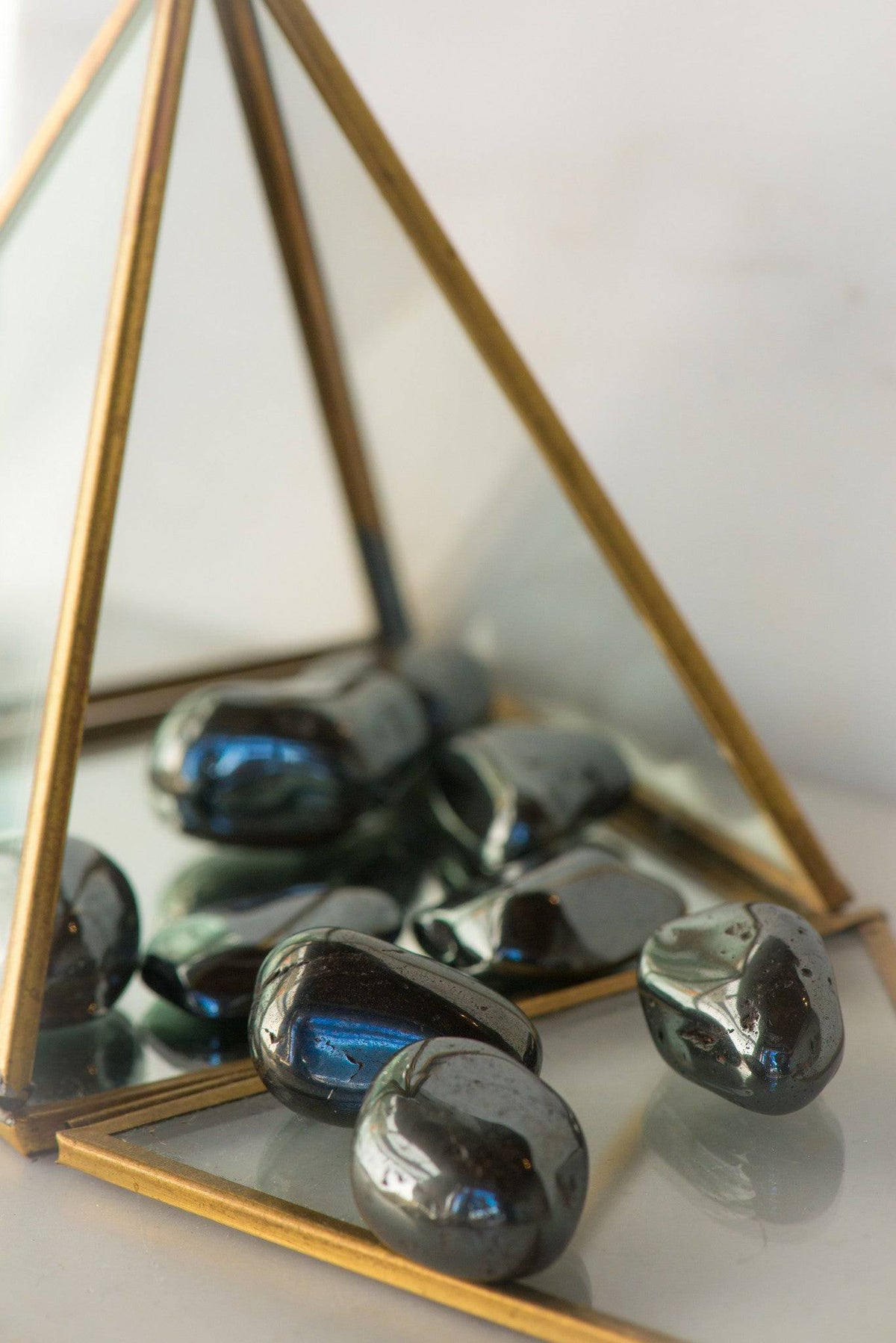 Smooth tumbled hematite stones from Sacred Light Soundbaths and Crystals, showing their metallic gray, polished surface.