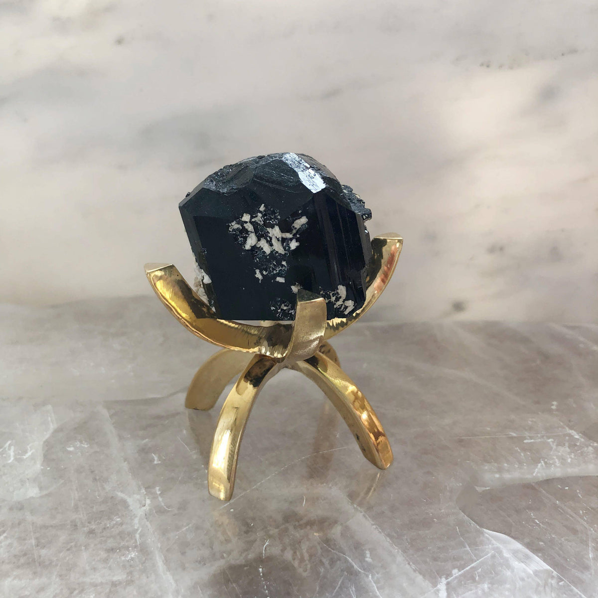 Black Tourmaline stone displayed on a brass stand, part of Sacred Light Soundbaths and Crystals' collection of healing stones.
